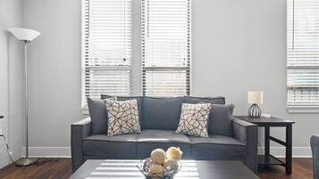 Un salon moderne avec un canapé gris, des coussins à motifs, une table basse agrémentée d’objets décoratifs et un lampadaire.