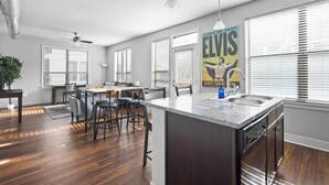 A modern kitchen with a central island, bar stools, and a dining area with a table and chairs. - The Residences at CityWay (Indianapolis)