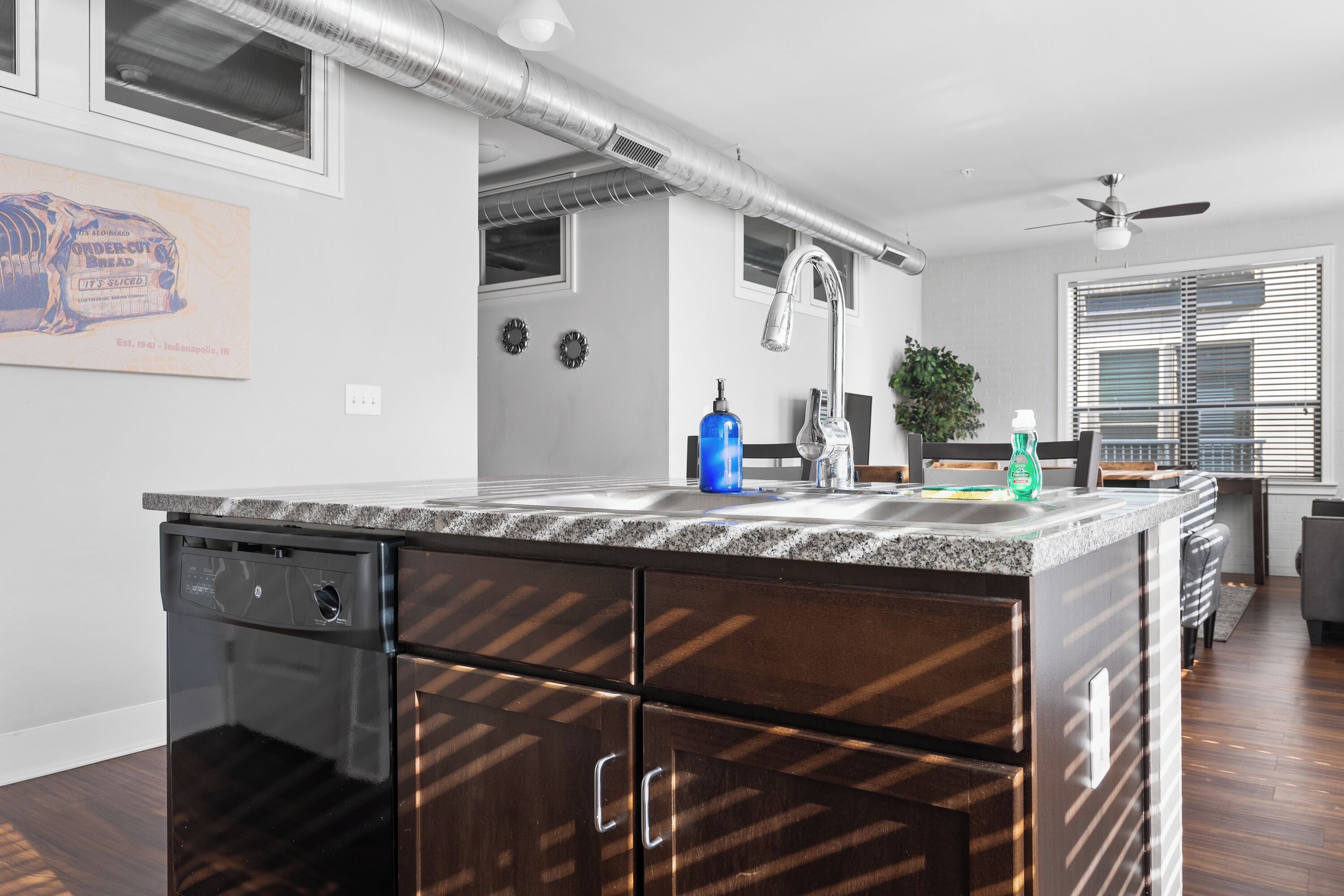 A modern kitchen with a built-in dishwasher, granite countertop, and a ceiling fan.