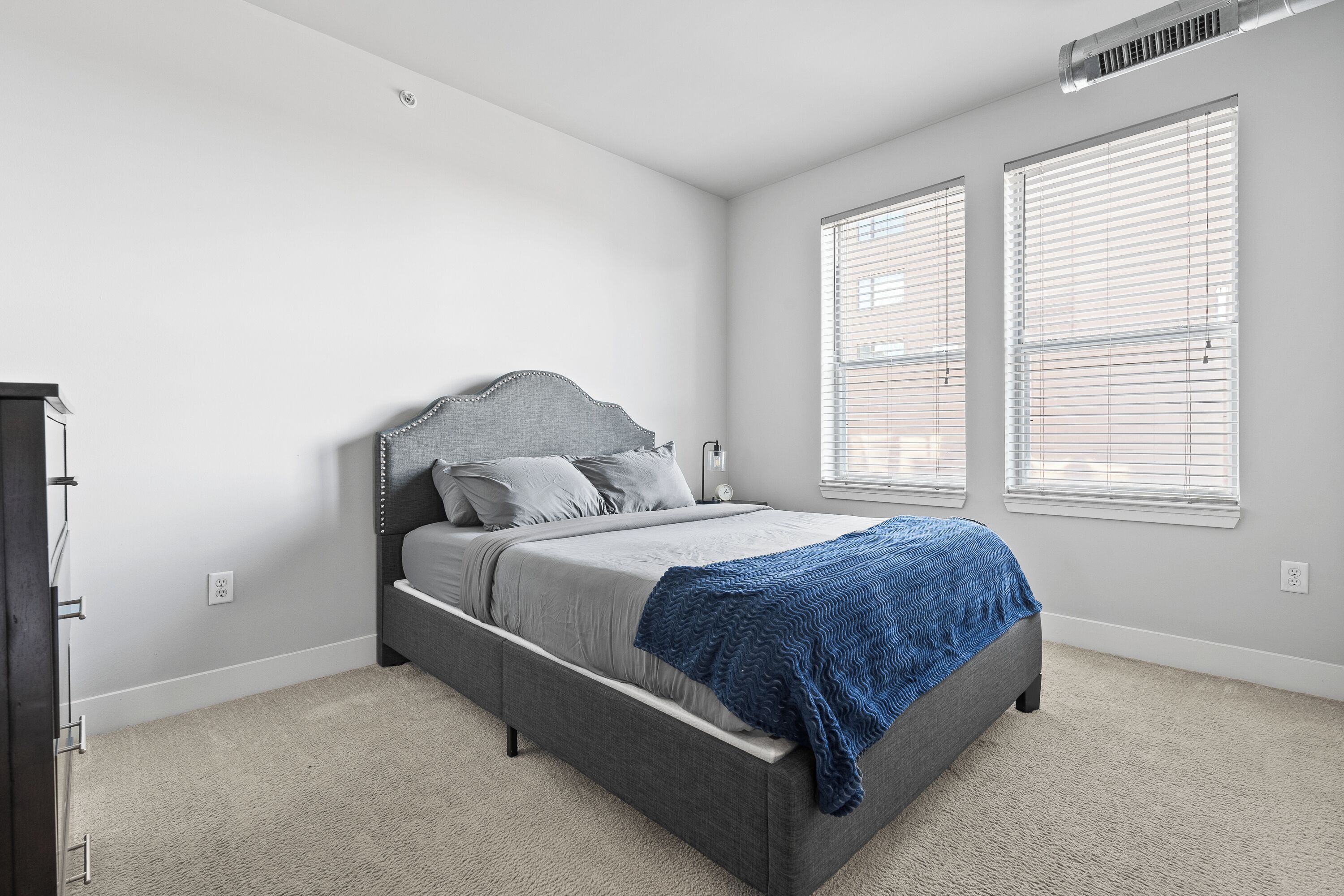 Un dormitorio con cama, cómoda y dos ventanas con persianas.