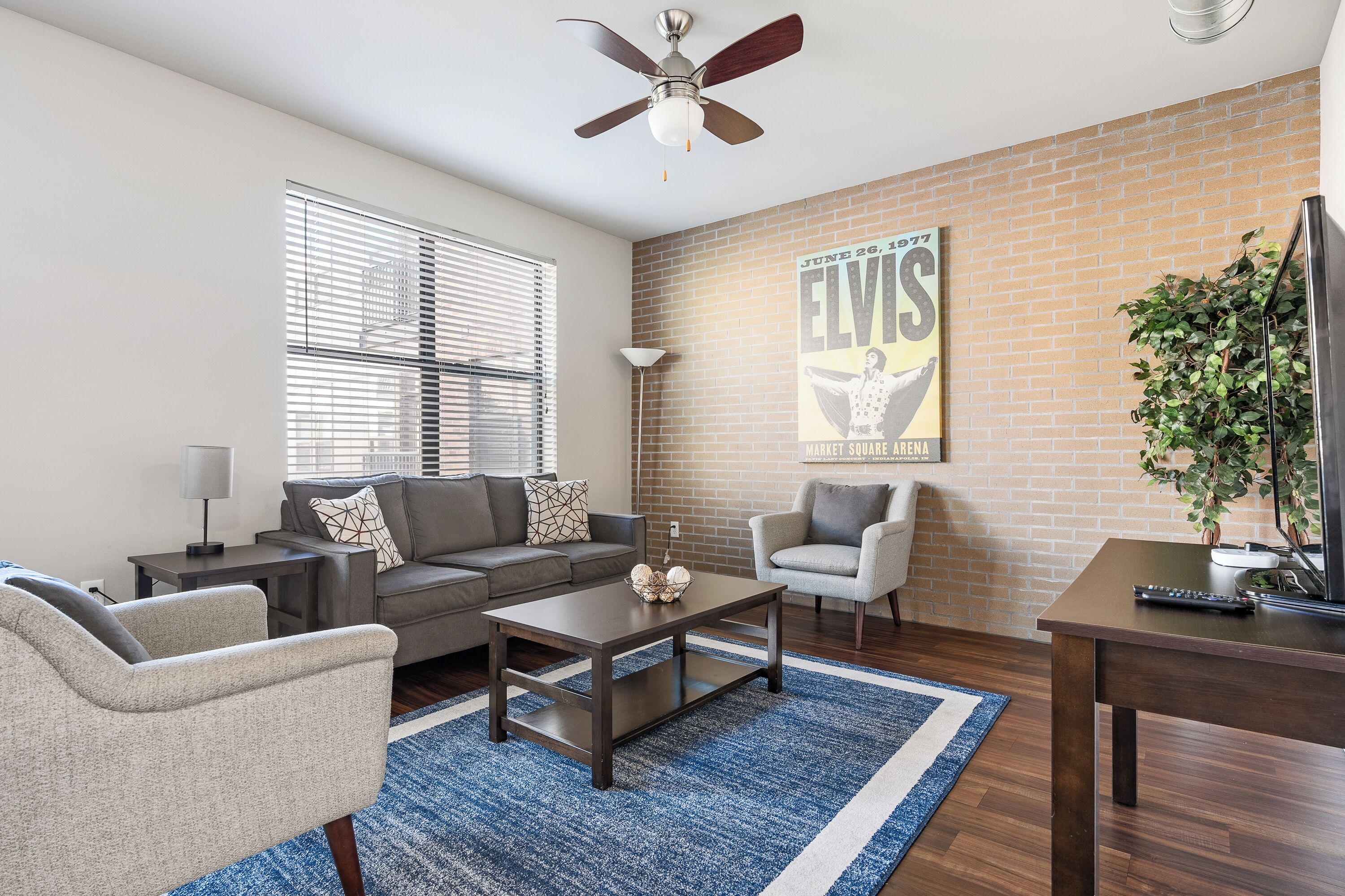 A living room with a sofa, armchairs, a coffee table, a TV, and a ceiling fan.