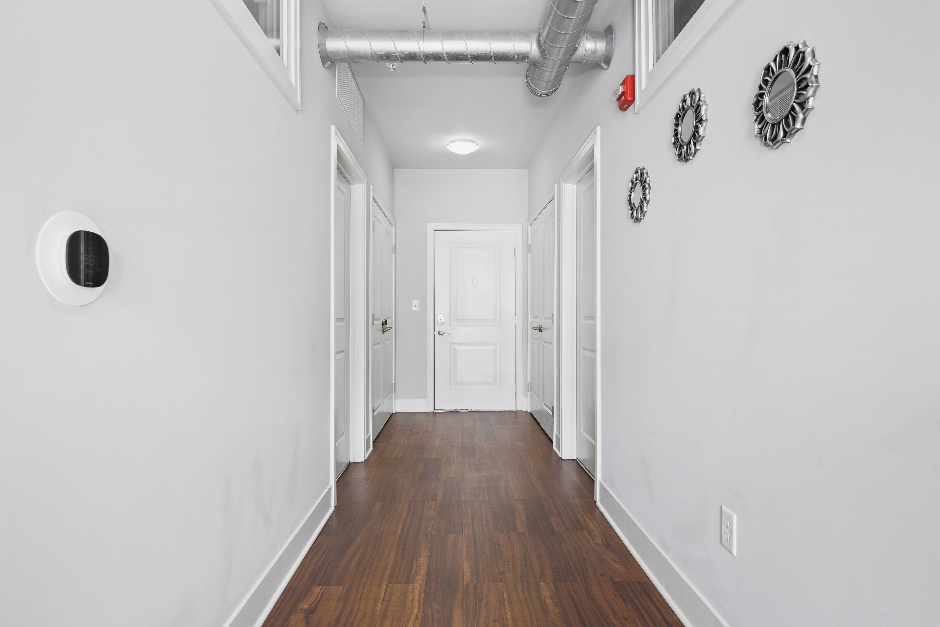 A hallway with wooden flooring, white walls, and a white door at the end.
