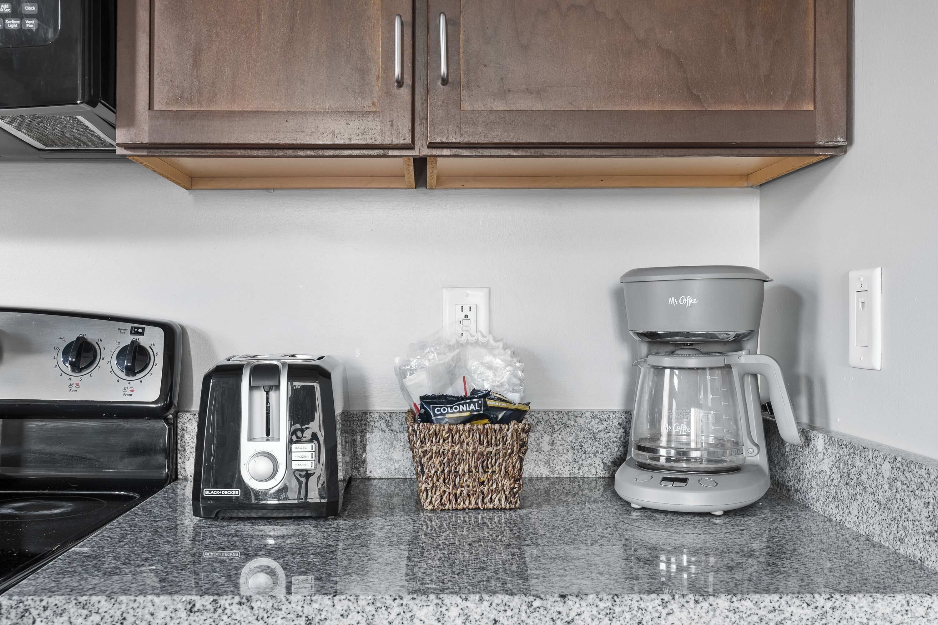 Eine Küche mit einem Toaster, einer Kaffeemaschine und einem Korb voller Gegenstände auf der Arbeitsfläche.