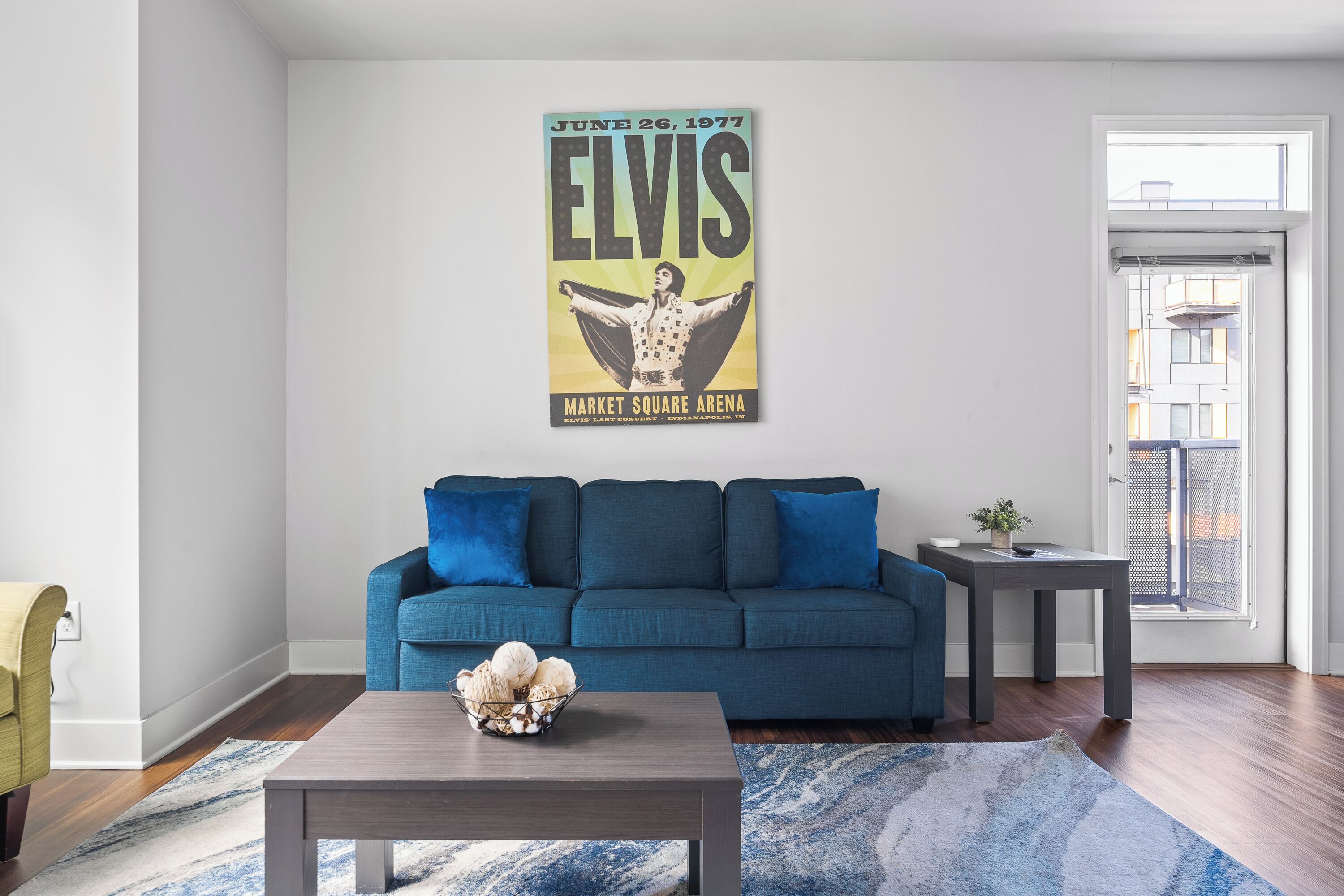 A living room with a blue sofa, a coffee table with a decorative bowl, and a poster on the wall.