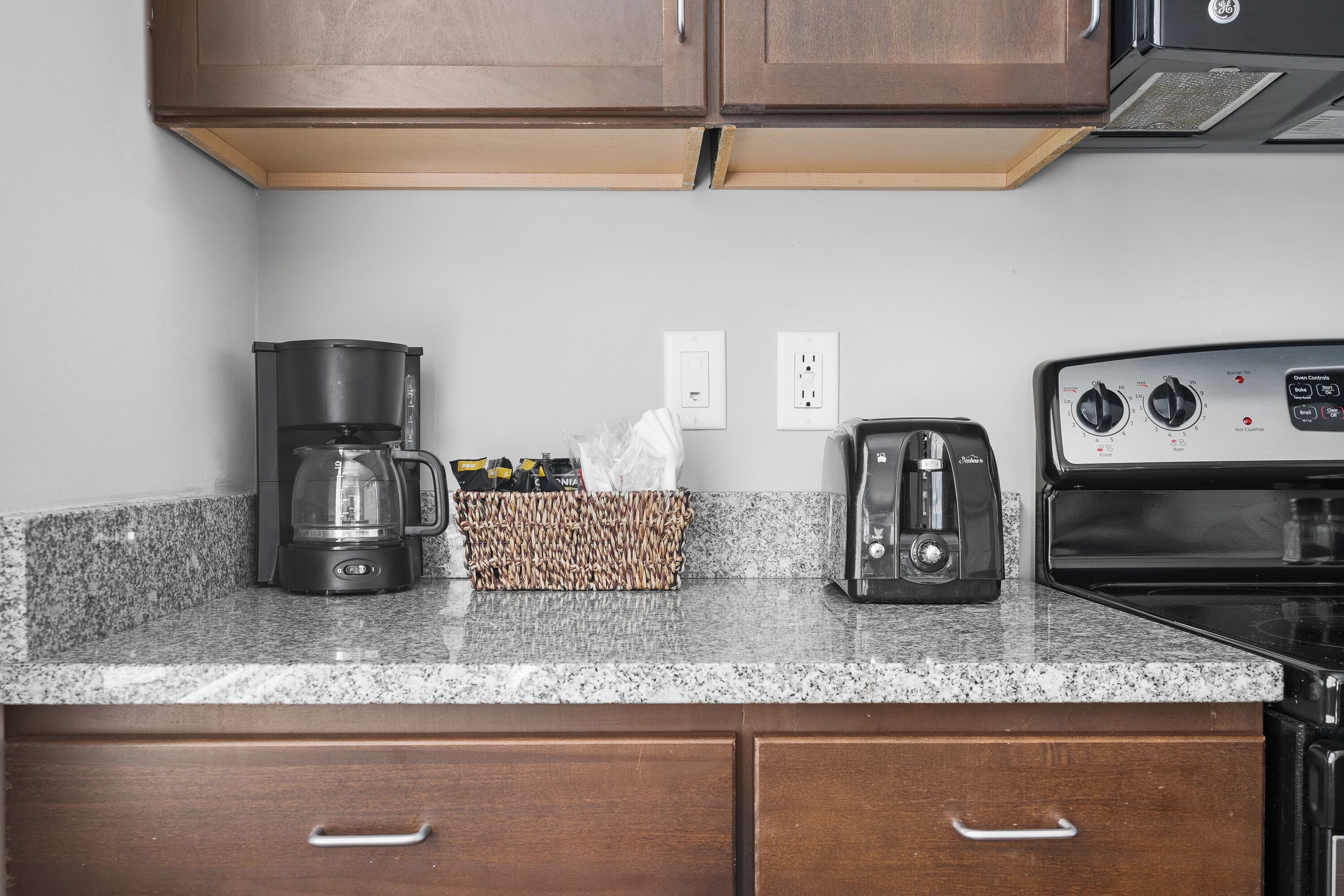 A kitchen with granite countertops, a coffee maker, a toaster, and a stove.