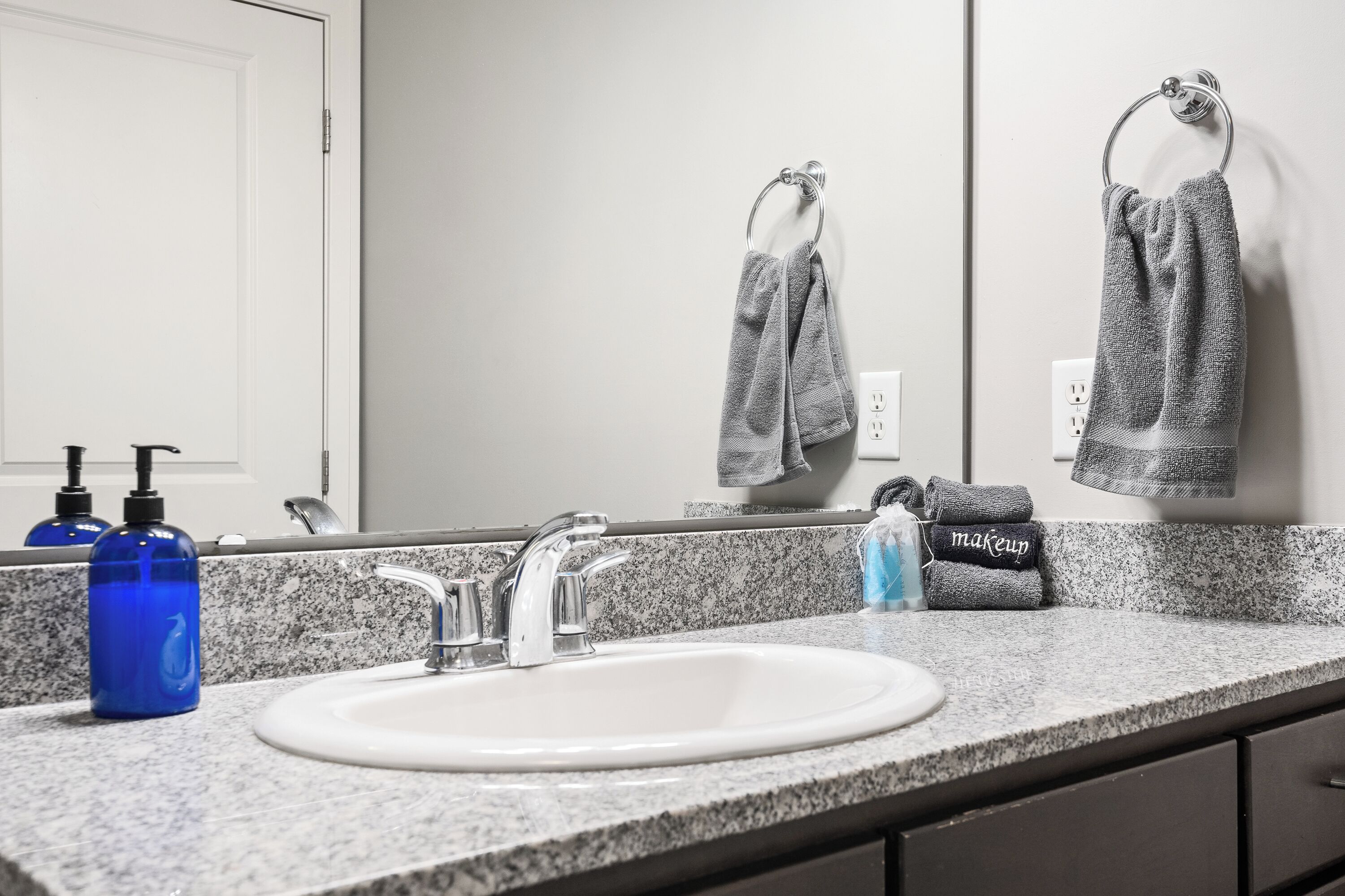 Un baño con encimera de granito, un lavabo blanco, un espejo y un perchero con toallas.