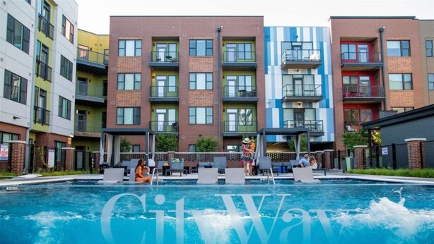 A swimming pool with lounge chairs and a covered seating area, surrounded by multi-story buildings with balconies. - The Residences at CityWay (Indianapolis)