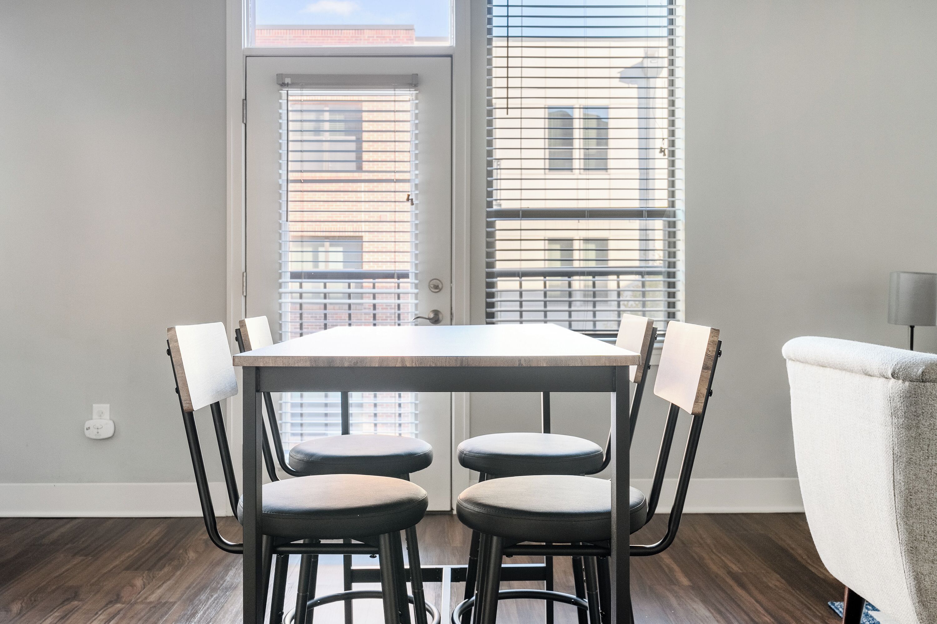 A dining area with a table and four chairs, a window with blinds, and a door.