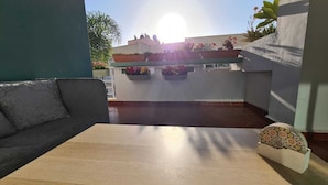 Ein modernes Wohnzimmer mit einem Holztisch, einem grauen Sofa und Blick auf ein Gebäude mit Pflanzen und Blumen.