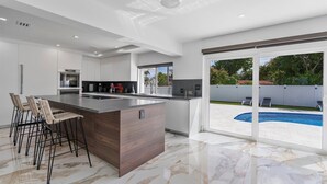 Una cocina moderna con una isla grande, taburetes de bar y vistas a una piscina en el patio.