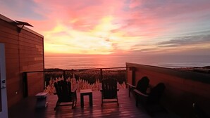 En træterrasse med stole og et bord, med udsigt til solnedgang over havet.