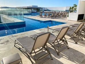 A rooftop pool area with lounge chairs and a glass-enclosed pool.