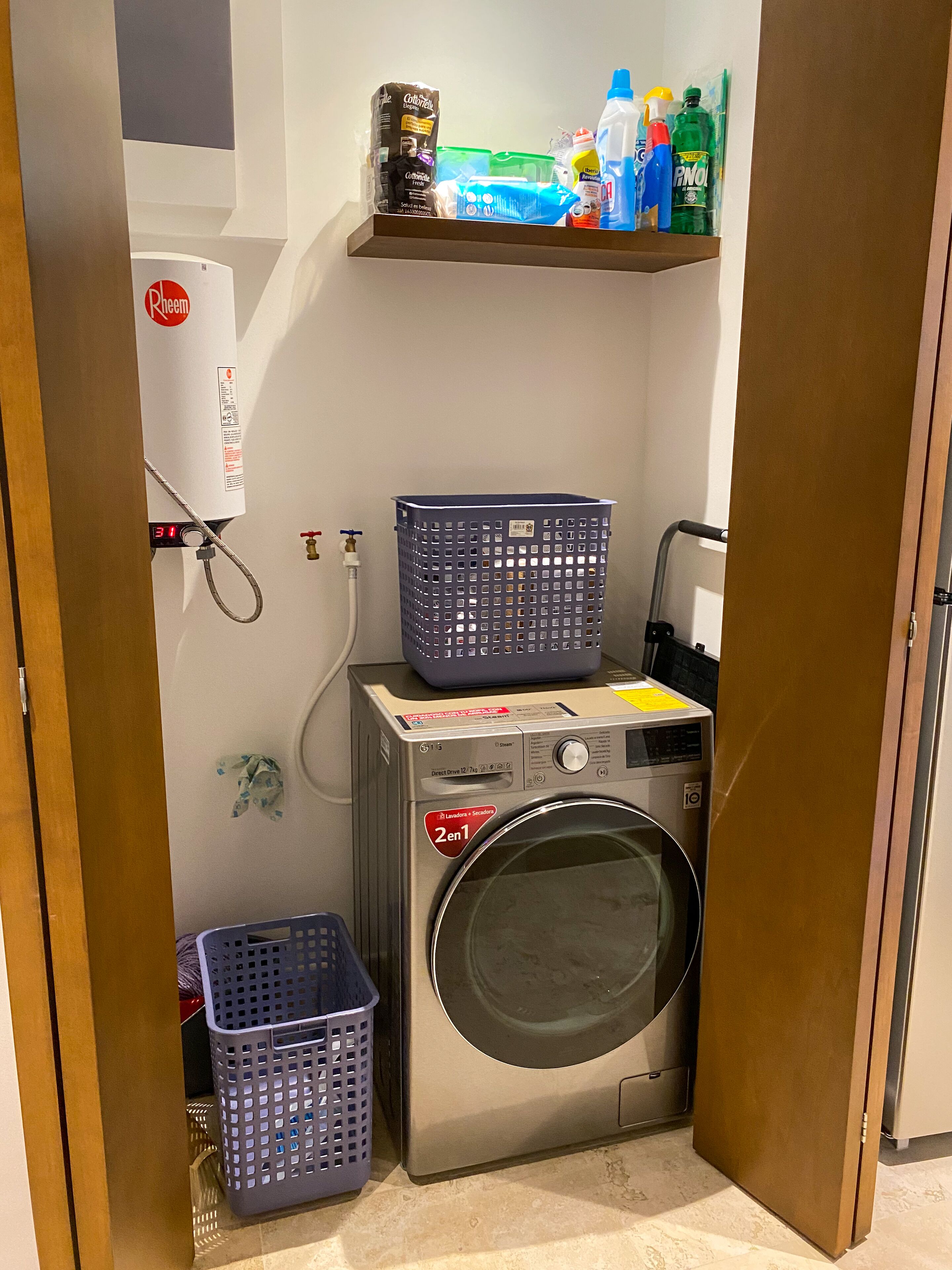 Een kleine wasruimte met een voorlader wasmachine, een droger en een plank met schoonmaakmiddelen.