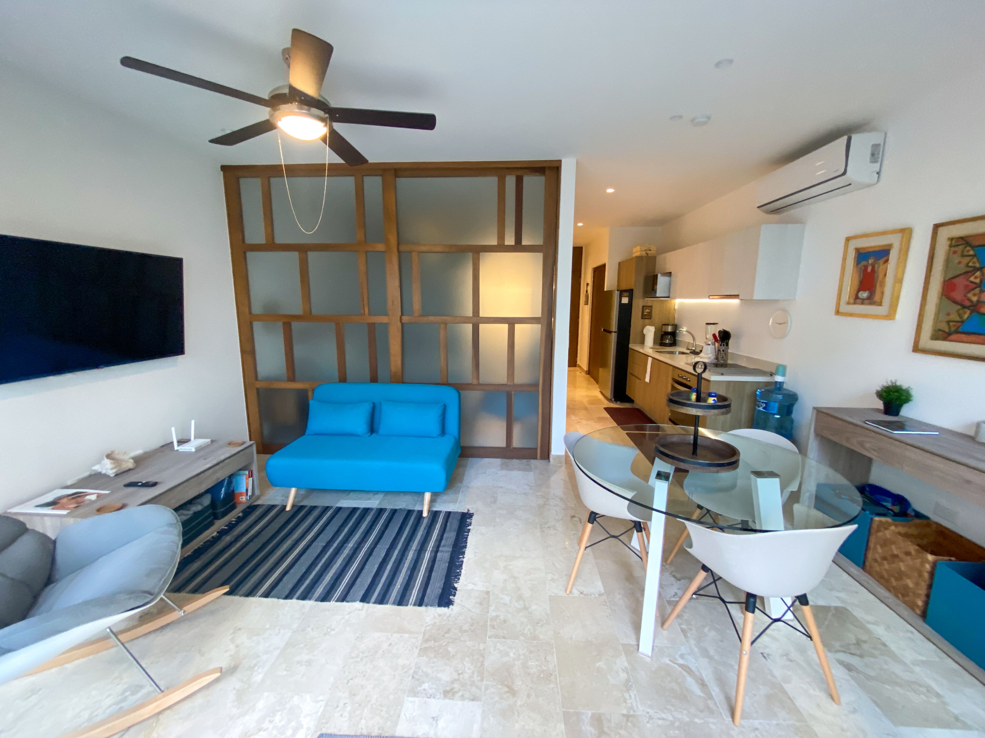 A modern living room with a blue sofa, a glass coffee table, and a ceiling fan.