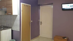 Une petite cuisine équipée d’un évier, de placards et d’un téléviseur fixé au mur.