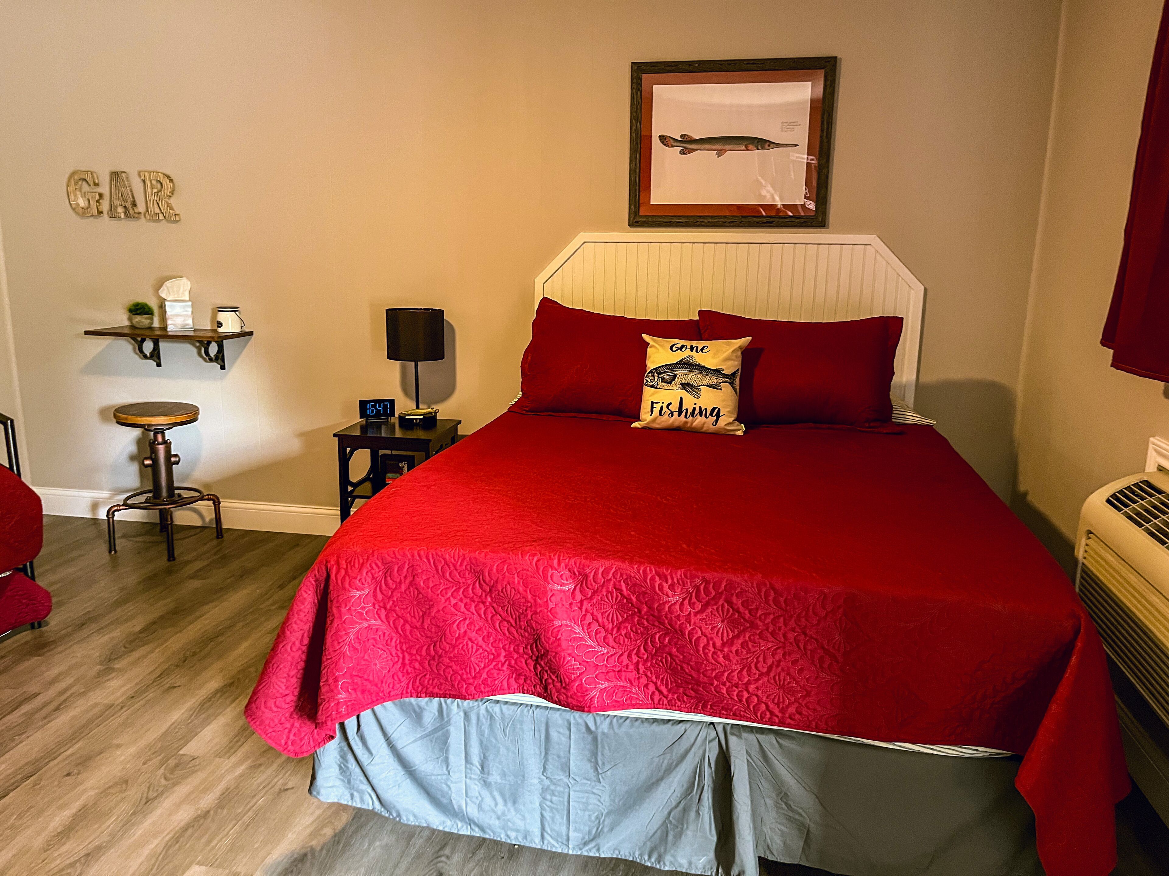 Un dormitorio con una cama grande, una mesita de noche con lámpara, un estante con objetos y un cuadro en la pared.
