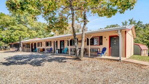 A row of single-story cabins with individual porches, each featuring a door and windows, set on a gravel ground with trees in the background.
