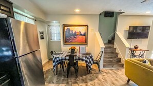 A modern kitchen with a stainless steel refrigerator, a dining area with a checkered tablecloth, and a staircase leading to a living area with a yellow armchair. - Reel Inn and Lodge (Quitman)