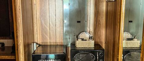 A compact room with wooden paneling, a small table with a radio, a refrigerator, and a mirror.