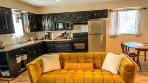 A modern kitchen with dark cabinets, a stainless steel refrigerator, and a yellow sofa with a cushion that says "enjoy today". - Reel Inn and Lodge (Quitman)
