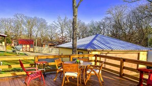 A wooden deck with a table and chairs, a red chair, and a small shed in the background.