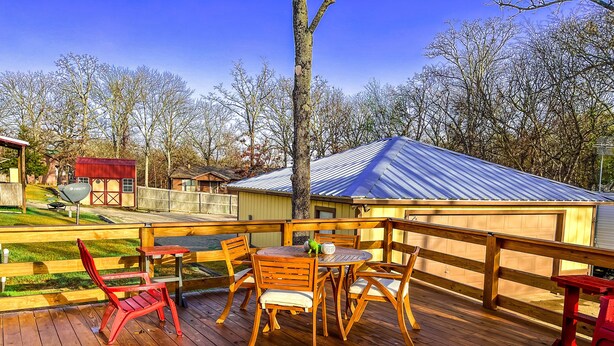 A wooden deck with a table and chairs, a red chair, and a small shed in the background. - Reel Inn and Lodge (Quitman)