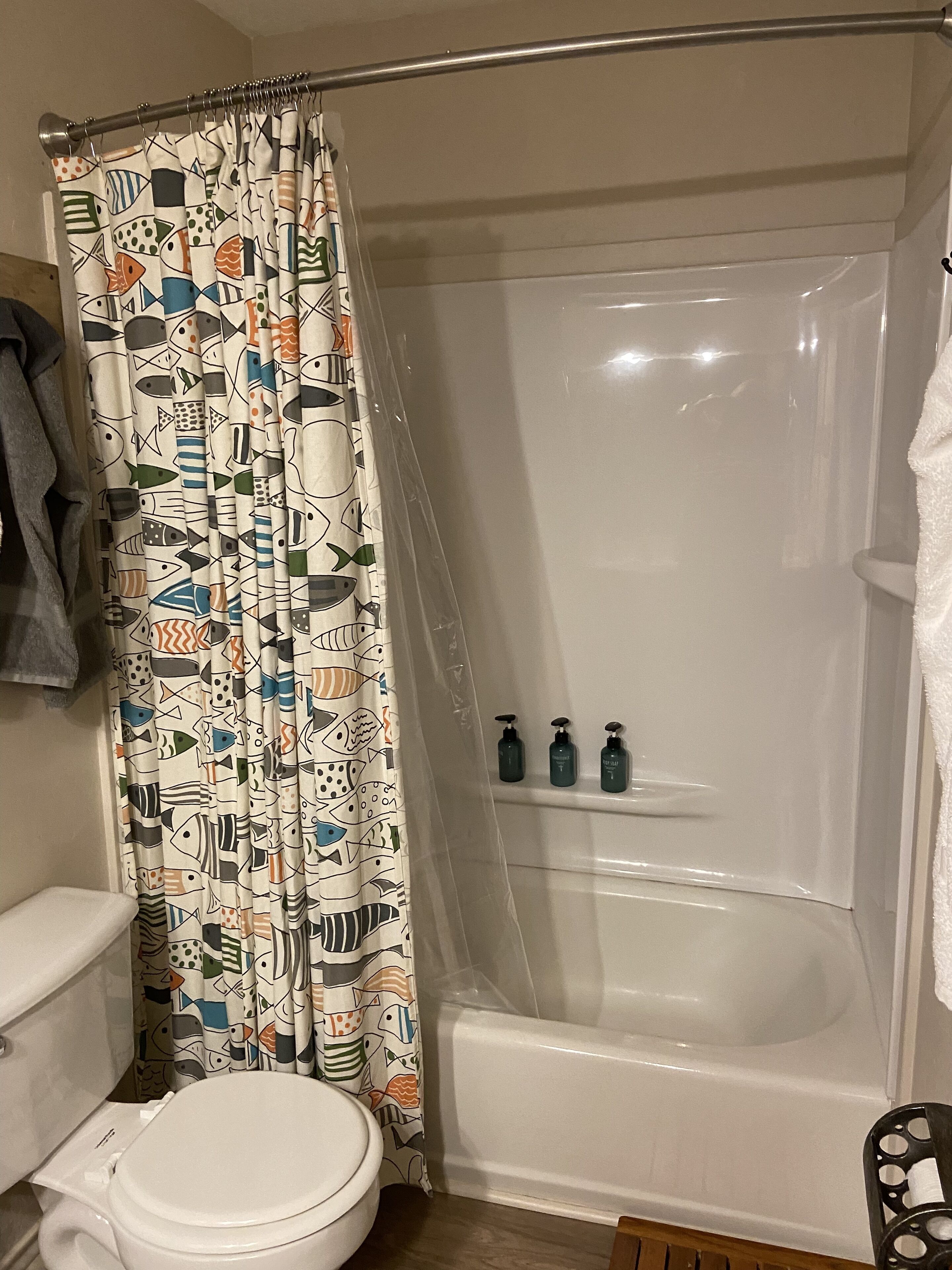 A bathroom with a toilet, a bathtub, and a shower curtain with a fish pattern.