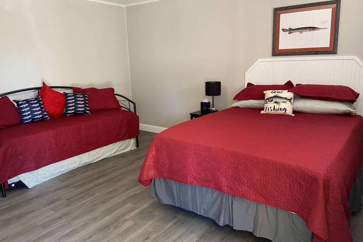 Un dormitorio con dos camas, cada una con ropa de cama roja y almohadas a rayas. Hay un cuadro en la pared sobre las camas.