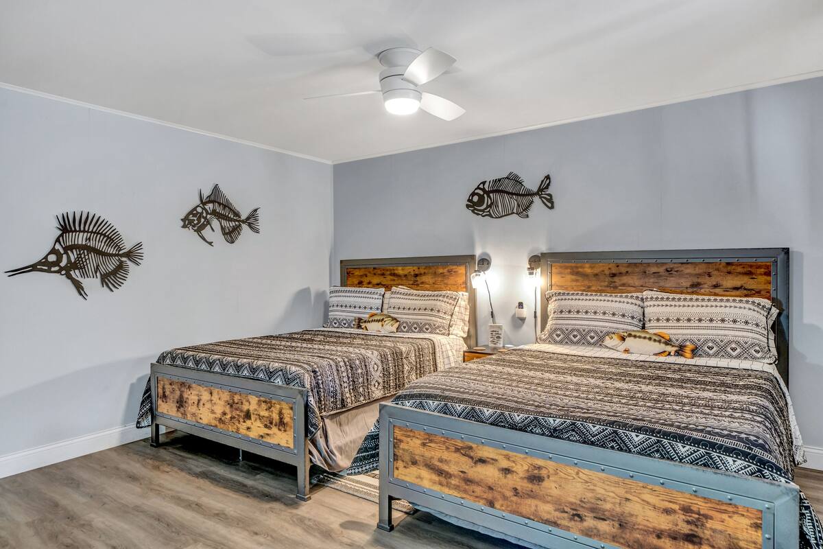 Un dormitorio con dos camas, ventilador de techo, adornos de peces en la pared y cabecera de madera.