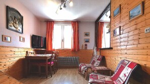 A cozy cabin interior with wooden walls, a dining area, a sofa, and a television. - Apartment T2, MOUNTAIN VIEW, center, ski, cures, close to cable cars and thermal baths (Bagnères-de-Luchon)