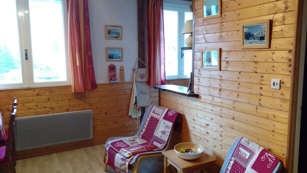 A cozy cabin room with wooden walls, a chair with a quilt, a small table with a bowl, and a window with curtains. - Apartment T2, MOUNTAIN VIEW, center, ski, cures, close to cable cars and thermal baths (Bagnères-de-Luchon)