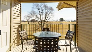 A covered outdoor area with a round table and four chairs, a metal railing, and a view of a tree and open field. - Lux 2BR Condo w/Jacuzzi, fast Wifi, Clubhouse, Gym (Branson)