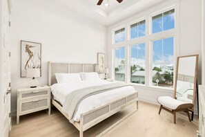 A bedroom with a large bed, two bedside tables, a chair, and a window with a view of houses.