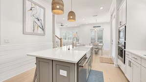 Une cuisine moderne avec des meubles blancs, un îlot central, des luminaires suspendus et un coin repas offrant une vue agréable.