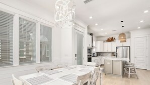 Une cuisine moderne avec des meubles blancs, un îlot central et un coin repas comprenant une table et des chaises blanches.