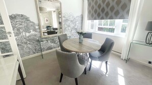 A dining area with a round table, two chairs, a vase with flowers, a mirror, and a window with patterned curtains. - Super Stylish Living in the Best Location in the Heart of Kensington (London)