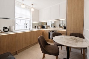 Cozinha moderna com armários de madeira, bancada de mármore e mesa de jantar redonda para dois.