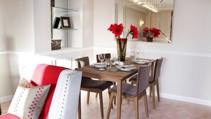 Un'area pranzo con un tavolo di legno apparecchiato per quattro persone, circondato da sedie. Uno specchio è appeso alla parete sopra il tavolo, riflettendo l'ambiente.