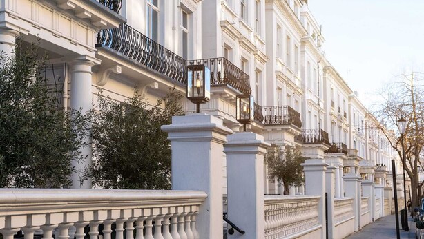 Filare di edifici bianchi con balconi, un recinto bianco e un marciapiede lastricato.