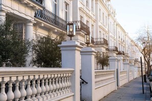 Una hilera de edificios blancos con balcones, una cerca blanca y un pavimento.