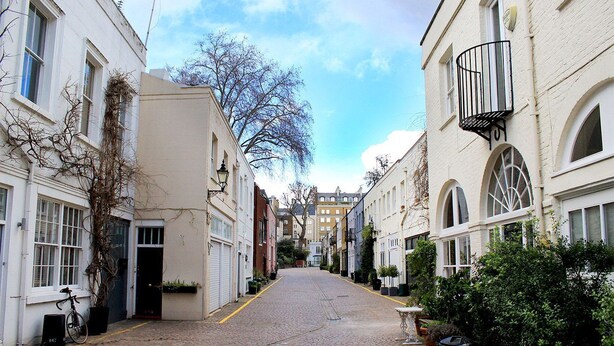 A narrow cobblestone street flanked by white buildings with arched windows and balconies.