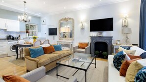 A modern living room with a sofa, coffee table, and fireplace. There is a kitchen area with a stove and sink.