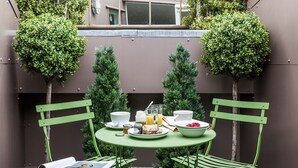 A small outdoor dining area with a round table, two green chairs, and a variety of food and drinks.