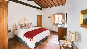 Ein Schlafzimmer mit einem Bettgestell aus Holz, einer roten Tagesdecke, einer hölzernen Kommode, einem Spiegel und einem gerahmten Bild an der Wand.