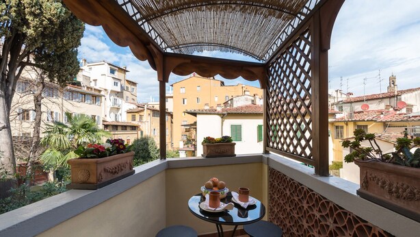 Ein Balkon mit Tisch für zwei Personen, umgeben von Topfpflanzen und einem dekorativen Gitter.