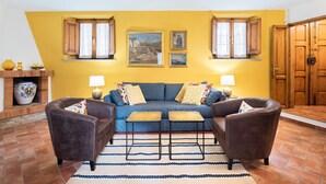 Ein Wohnzimmer mit einem blauen Sofa, zwei Sesseln, einem gemusterten Teppich und einem Kamin mit Dekorationen.