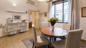 A dining area with a round table, four chairs, a vase with flowers, a coffee machine, and a wall-mounted air conditioner. - Perfect Florence Location-Upscale Historic-AC-2 Bathrooms-Lift-Washer (Florence)