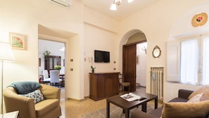 A living room with a sofa, a coffee table, and a TV. There is a dining area in the background with a table and chairs. - Perfect Florence Location-Upscale Historic-AC-2 Bathrooms-Lift-Washer (Florence)