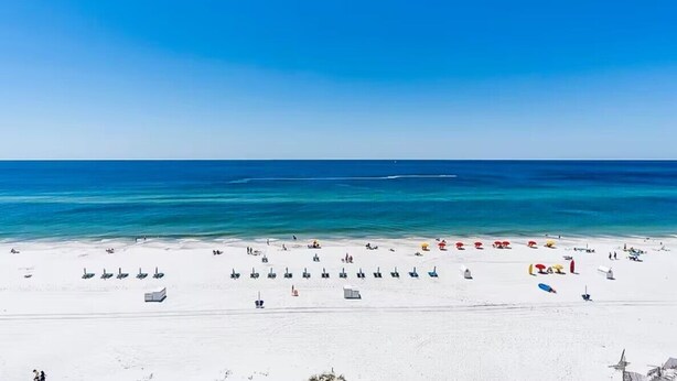 Una spiaggia con sabbia bianca e acqua cristallina. Si vedono diversi ombrelloni e sdraie.