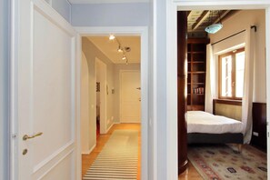 A hallway leading to a bedroom with a bed, a window, and a bookshelf.